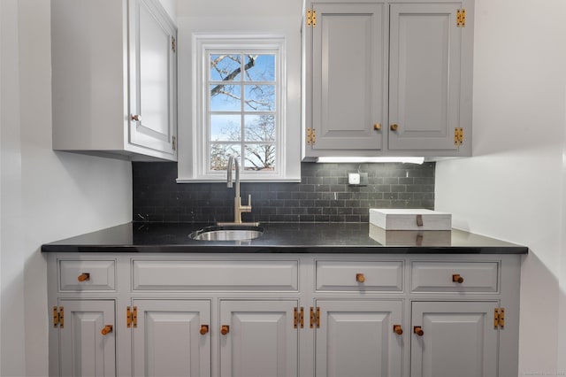 kitchen with dark countertops, white cabinetry, a sink, and backsplash