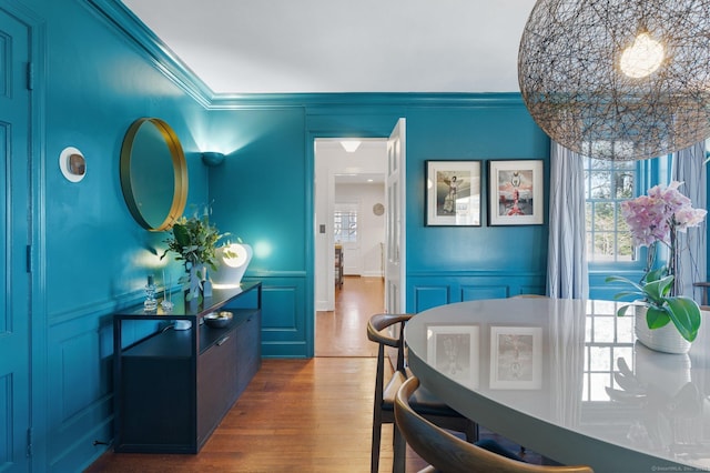 dining space with ornamental molding, wood finished floors, and a decorative wall