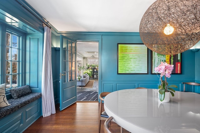 dining area with dark wood-style floors, a decorative wall, and ornamental molding