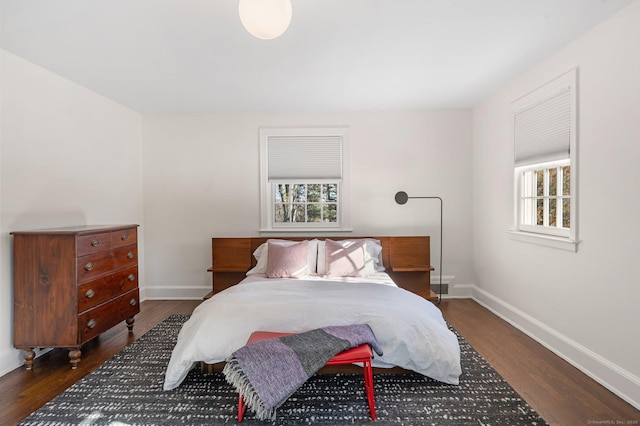 bedroom with multiple windows, dark wood finished floors, and baseboards