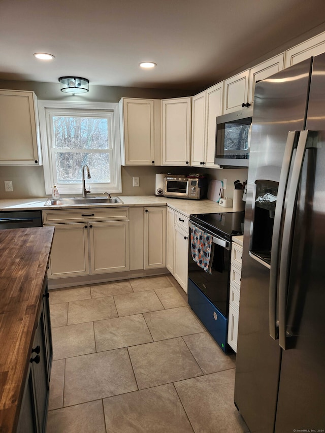 kitchen featuring light tile patterned flooring, sink, butcher block countertops, and black appliances