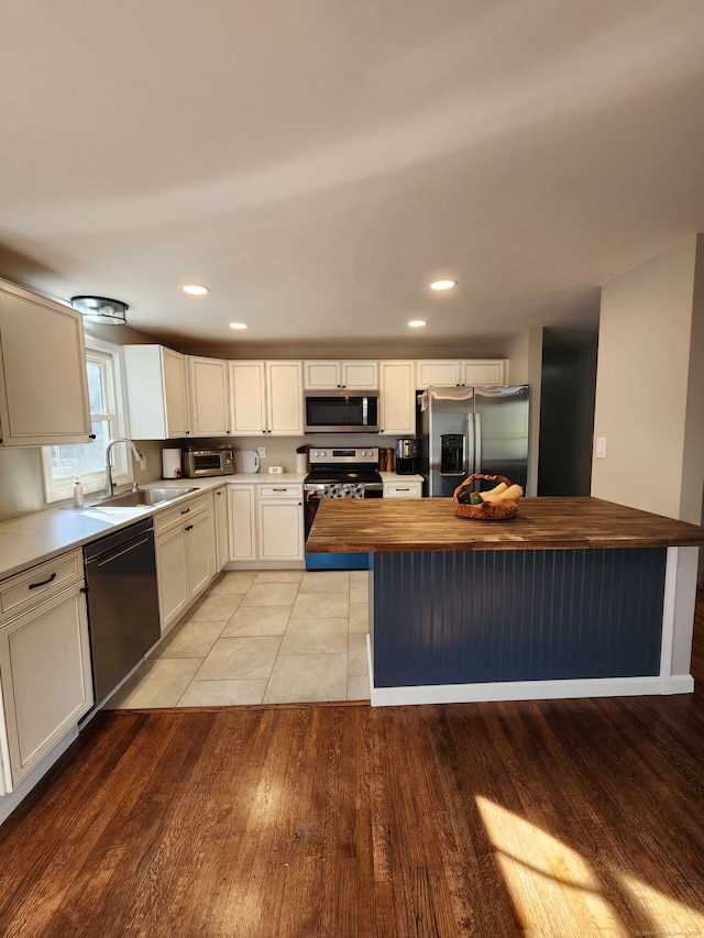 kitchen featuring sink, butcher block countertops, light hardwood / wood-style floors, white cabinets, and appliances with stainless steel finishes