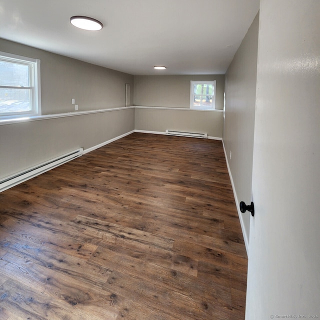 unfurnished room featuring plenty of natural light, baseboard heating, and dark wood-type flooring