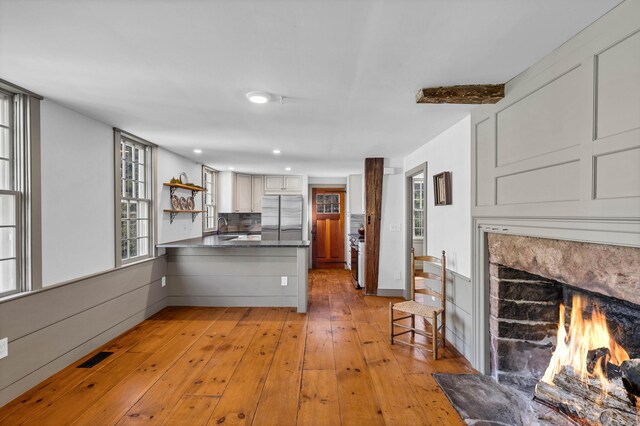 kitchen featuring kitchen peninsula, sink, light hardwood / wood-style flooring, white cabinetry, and stainless steel refrigerator