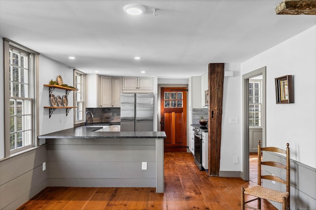 kitchen featuring dark wood-type flooring, sink, decorative backsplash, kitchen peninsula, and stainless steel appliances