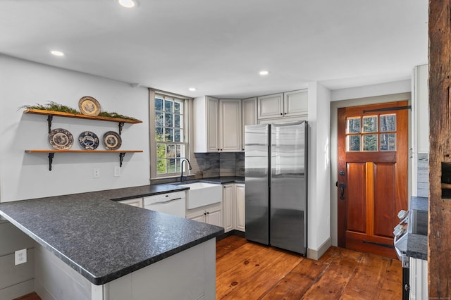 kitchen featuring dishwasher, sink, dark hardwood / wood-style flooring, kitchen peninsula, and stainless steel refrigerator