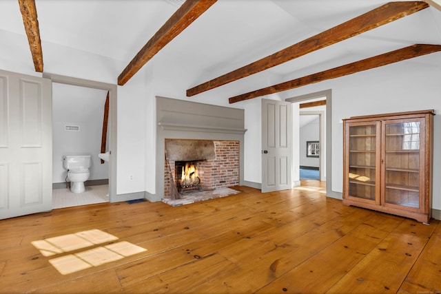 unfurnished living room featuring hardwood / wood-style flooring, beam ceiling, and a fireplace