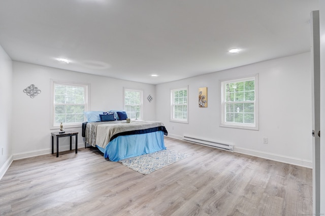 bedroom with light wood-type flooring, multiple windows, and a baseboard heating unit