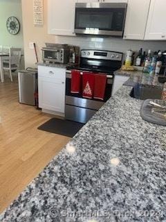 kitchen featuring light stone countertops, light hardwood / wood-style flooring, white cabinets, and appliances with stainless steel finishes