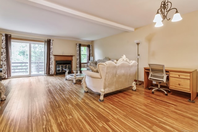 living room with a chandelier, wood finished floors, beam ceiling, a desk, and a glass covered fireplace