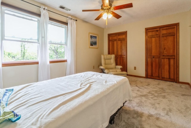 bedroom with light carpet, baseboards, two closets, and ceiling fan