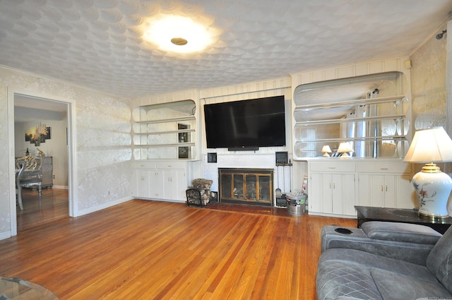 living room with built in features, a textured ceiling, hardwood / wood-style flooring, and a brick fireplace