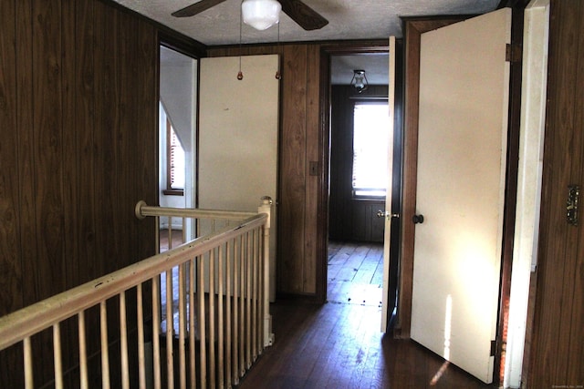 hallway featuring wooden walls, a textured ceiling, and dark hardwood / wood-style floors