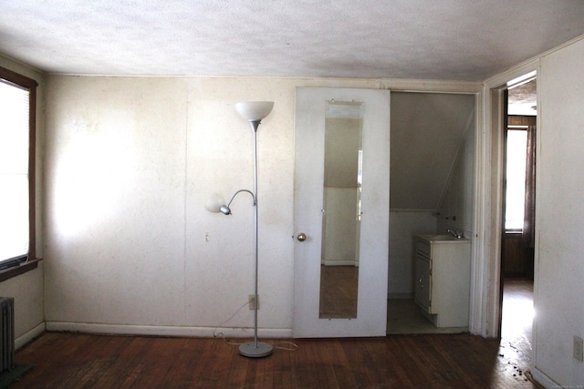 interior space with a textured ceiling, dark wood-type flooring, and radiator