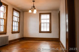 unfurnished dining area featuring hardwood / wood-style flooring, radiator, and a chandelier