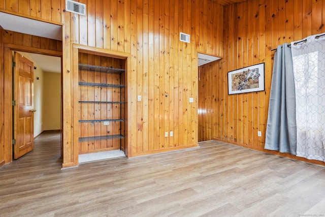 unfurnished room with light hardwood / wood-style floors and wooden walls