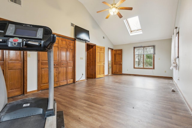 exercise room with a skylight, ceiling fan, hardwood / wood-style floors, and high vaulted ceiling