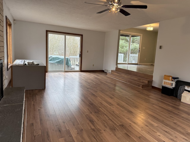 unfurnished living room featuring a wealth of natural light, ceiling fan, a large fireplace, and dark hardwood / wood-style floors