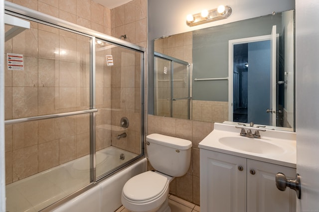 full bathroom featuring bath / shower combo with glass door, tile walls, toilet, and vanity