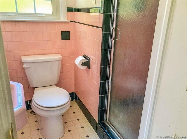 bathroom featuring tile patterned floors, toilet, a shower with shower door, and tile walls