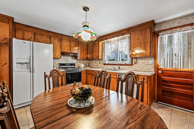 kitchen with pendant lighting, stove, white refrigerator with ice dispenser, light tile patterned floors, and tasteful backsplash