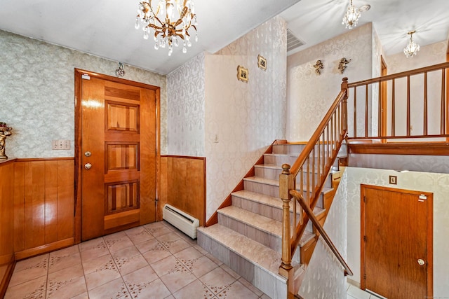 tiled foyer entrance with wood walls, a baseboard heating unit, and a notable chandelier