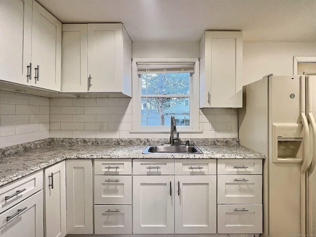 kitchen featuring light stone countertops, tasteful backsplash, sink, white refrigerator with ice dispenser, and white cabinets