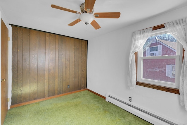 empty room featuring carpet, ceiling fan, baseboard heating, and wood walls