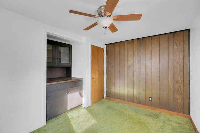 unfurnished bedroom with carpet, ceiling fan, and wood walls