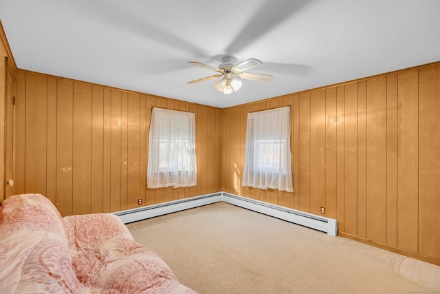 unfurnished room with carpet, ceiling fan, wood walls, and a baseboard heating unit