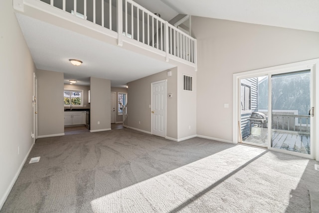 unfurnished living room with sink, high vaulted ceiling, and carpet