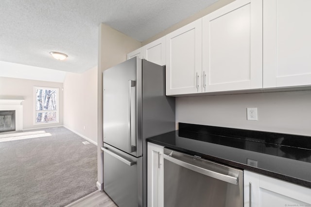 kitchen with stainless steel appliances, light carpet, white cabinets, and a textured ceiling