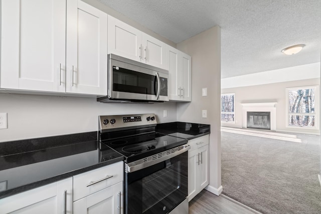 kitchen featuring white cabinetry, light colored carpet, stainless steel appliances, and a textured ceiling