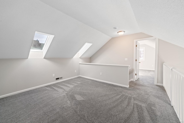 additional living space featuring vaulted ceiling with skylight, carpet floors, and a textured ceiling