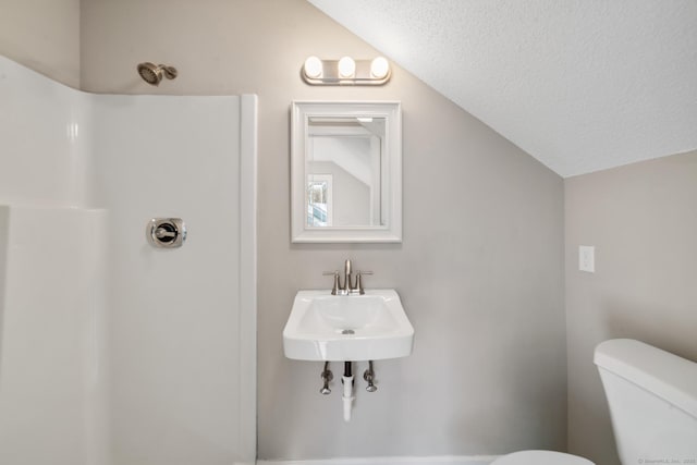 bathroom featuring lofted ceiling, sink, a textured ceiling, and toilet