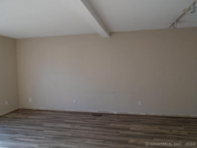 empty room featuring beam ceiling and dark wood-type flooring