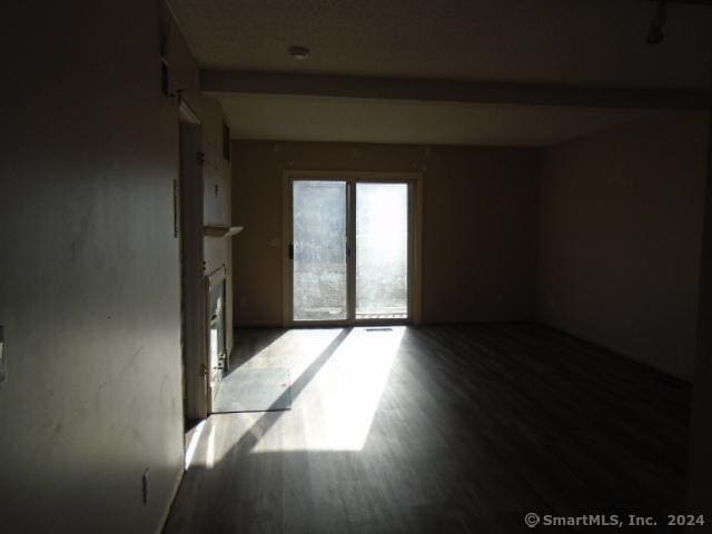 spare room featuring beamed ceiling and wood-type flooring