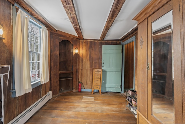 empty room featuring hardwood / wood-style flooring, a healthy amount of sunlight, a baseboard radiator, beamed ceiling, and wood walls