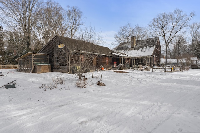 snow covered back of property featuring a garage and a chimney