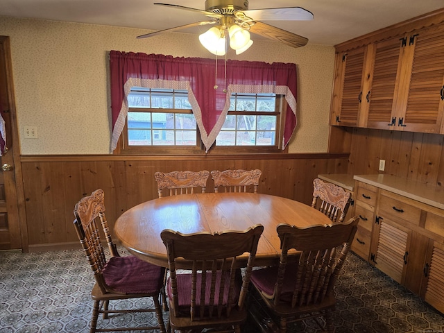 dining area featuring ceiling fan and wood walls