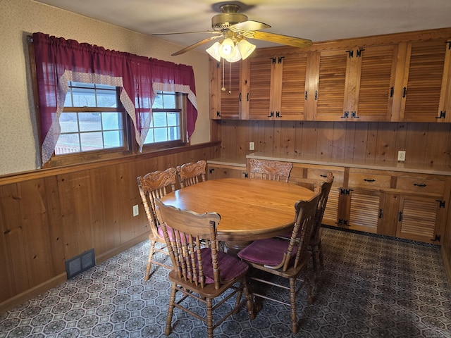 dining space with ceiling fan and wood walls