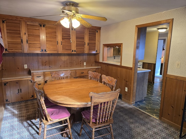 dining space featuring ceiling fan and wood walls