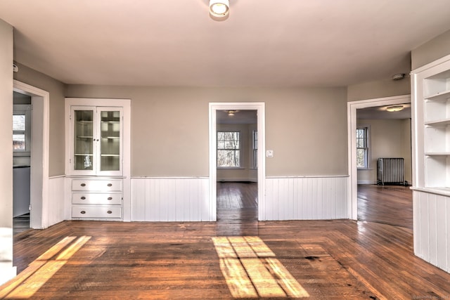 unfurnished room featuring built in shelves, radiator heating unit, and dark wood-type flooring