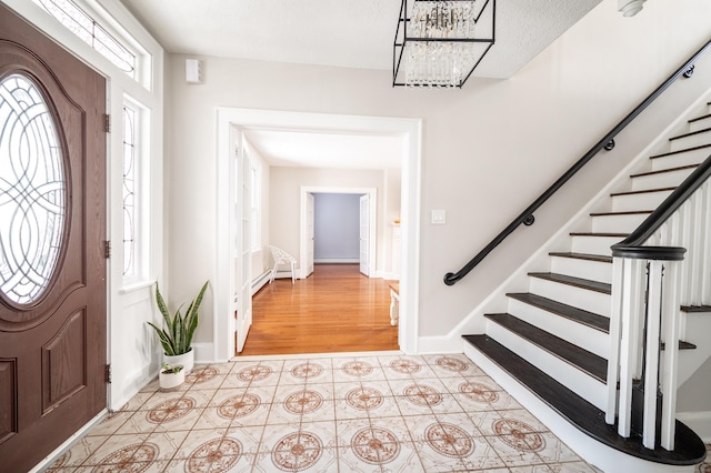 tiled entrance foyer featuring baseboard heating, plenty of natural light, and an inviting chandelier