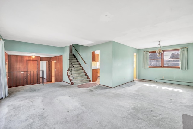 unfurnished living room with a baseboard heating unit, carpet floors, and stairway