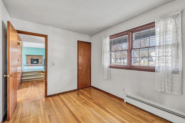 unfurnished bedroom featuring light wood-type flooring, a baseboard heating unit, a closet, a fireplace, and baseboards