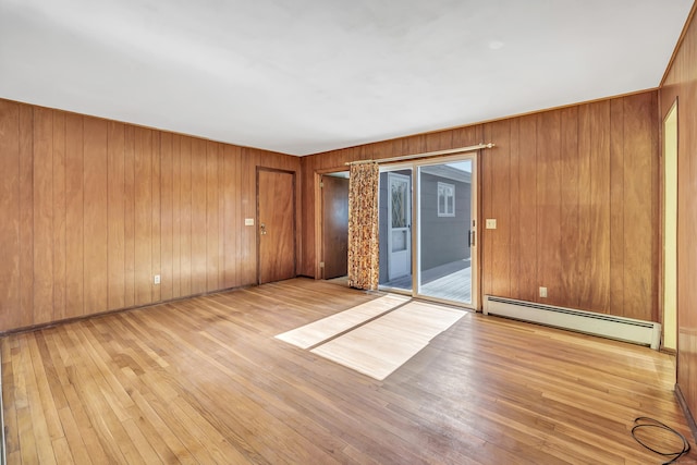 empty room featuring baseboard heating, wood walls, and light wood finished floors