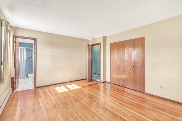 unfurnished bedroom with a baseboard heating unit, baseboards, light wood-style floors, a closet, and ensuite bath