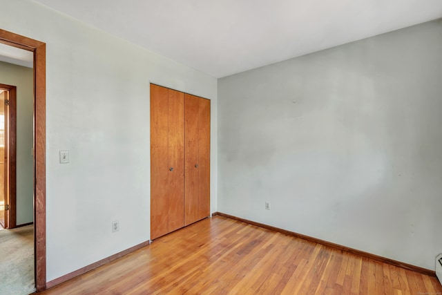 unfurnished bedroom featuring light wood finished floors, baseboards, and a closet