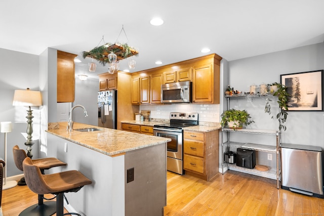 kitchen with appliances with stainless steel finishes, tasteful backsplash, light stone counters, sink, and a breakfast bar area